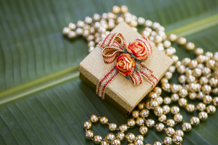 Christmas present on green banana leaf background, gold color gift box and golden beadsの写真素材