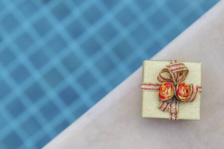Gold color gift box with paper rose flower with space on swimming pool background