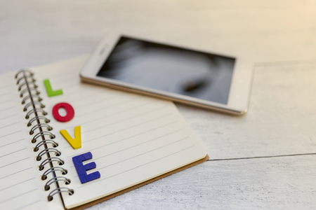 Valentine concept, colorful wooden love text over blank notebook with blurry smartphone, selective focus, vintage styleの写真素材