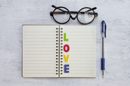 Colorful love on blank notebook with pen and eyeglasses on white texture backgroundの写真素材