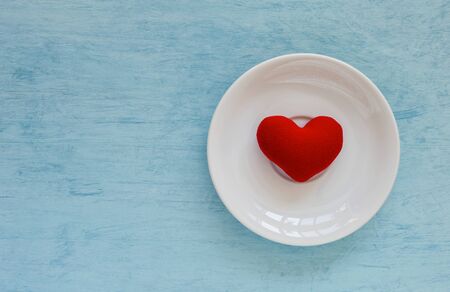 Red heart on white ceramic plate over blue texture backgroundの写真素材