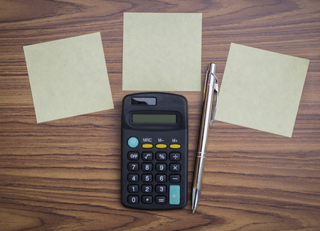 Blank notepad and calculator with silver pen on wood background, business concept