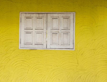 Architecture detail, yellow cement wall texture and old white wooden windowの写真素材