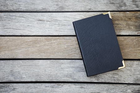 Old black leather cover book on wood background, outdoor day lightの写真素材
