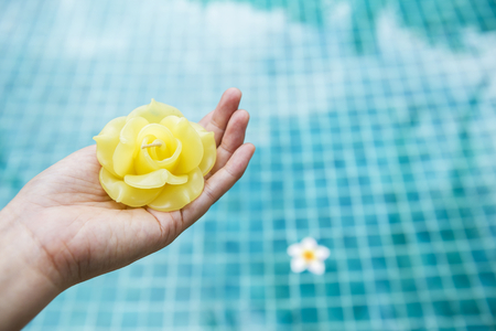 Beautiful yellow rose candle in girl hand over blurred blue swimming pool background, spa decoration conceptの写真素材