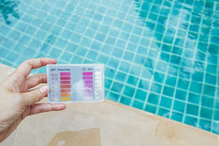 Girl hand holding water testing test kit over swimming pool backgroundの写真素材