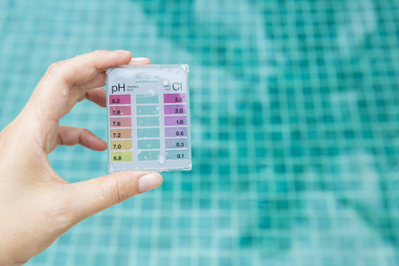 Girl hand holding mini water testing test kit over blue swimming pool water background, summer outdoor day lightの写真素材