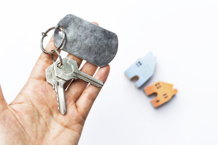 Girl hand holding hose key over blurred miniature house on white background, property and real estate conceptの写真素材