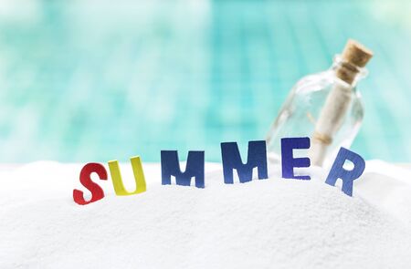 Summer concept background, colorful wooden text on white sand over blurred blue water backgroundの写真素材