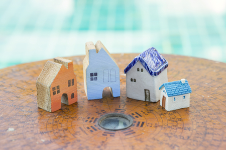 House feng shui concept, beautiful miniature house on ancient wooden feng shui compass over blurred blue water backgroundの写真素材