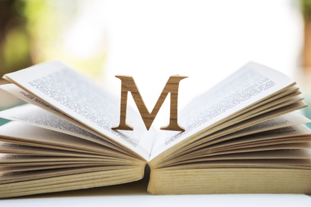 Wooden M font design on open old book over blurred background, outdoor day lightの写真素材