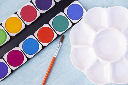 Closeup watercolor palette in flower shape and colorful watercolor tablet on blue table backgroundの写真素材