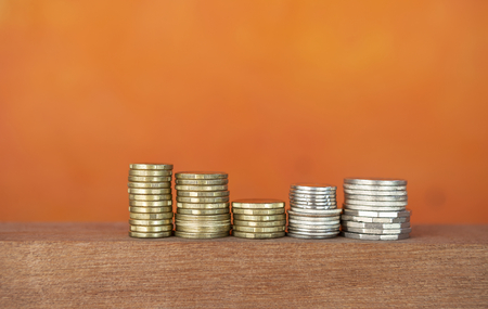 Stack of gold and silver coins over blurred orange background, banking and financial conceptの写真素材