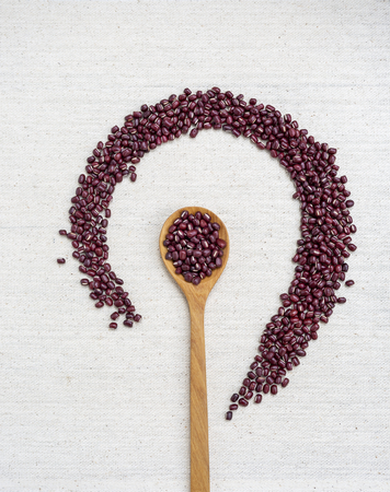 Organic small red beans display with wooden spoon on canvas texture background