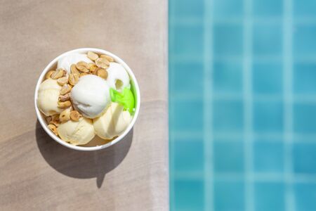 Coconut cream ice cream with peanut topping on the swimming edge with space on blurred blue water background, summer outdoor day lightの写真素材