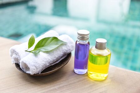 Spa concept background, Massage oil in glass bottle with white hand towel on swimming pool edge with...