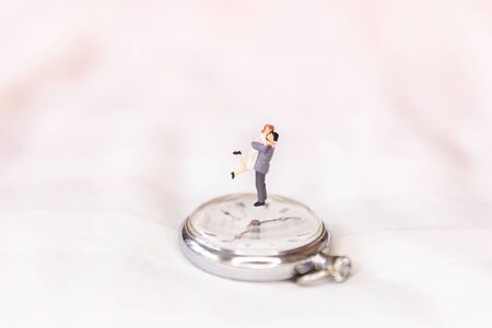 Miniature happy couple on vintage watch over blurred background, wedding and aniversary concept,...