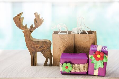 Christmas concept, Wood reindeer with blurred gift and gift in brown shopping bag over blurred blue water background, Christmas giftの写真素材