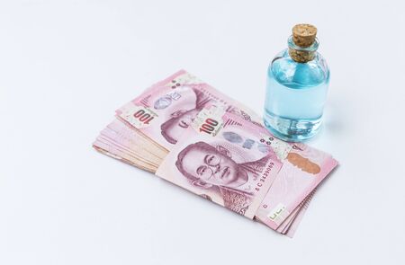 Ethanol alcohol in glass bottle with Thai bank note on white background, buy and sale concept, cleaning and hygiene productの写真素材