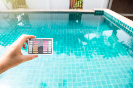 Water test kit in girl hand over blurred clear swimming pool water background, summer outdoor day light, water quality check, pool maintenanceの写真素材