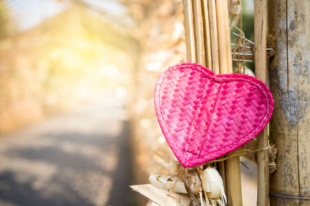 Pink bamboo wooden heart on bamboo fence with vintage warm light, love and romance symbol, valentine concept, outdoor day lightの写真素材