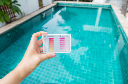 Water testing test kit in girl hand over blurred swimming pool background, summer outdoor day light, water check kitの写真素材