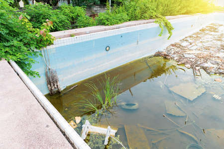 Abandoned outdoor public swimming pool in Thailand, environmental pollution, outdoor day light, dirty water kept in old swimming pool with garbageの写真素材