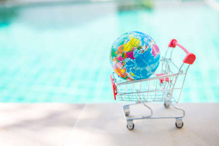 Earth global in shopping cart over blurred blue water background, outdoor day light, online shoppingの写真素材