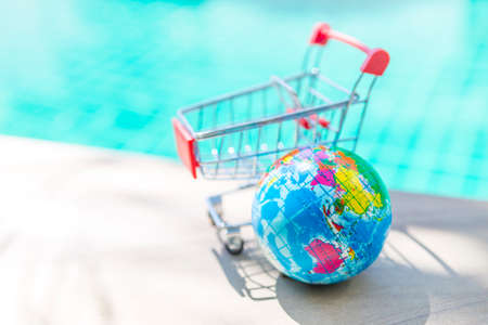 New global online shopping concept, world hand stress releif massage ball with empty shopping cart on swimming pool edge, outdoor day brith lightの写真素材