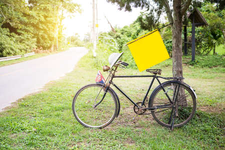 Old bicycle under the tree with yellow sign on the side road, countryside life style in northern Thailandの写真素材
