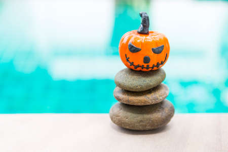 Halloween pumpkin with funny face on stack of stone over blurred blue water background, outdoor day light, happy halloween conceptの写真素材