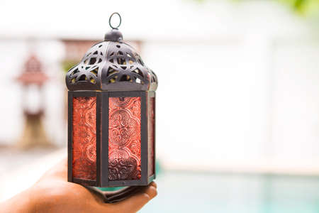 Simple design moroccan metal lamp in clay hand over blurred outdoor background, indoor house...
