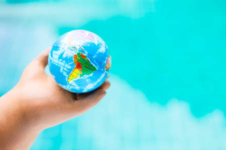 World map on global ball in clay hand over blurred blue water background, global warming and environmentalの写真素材