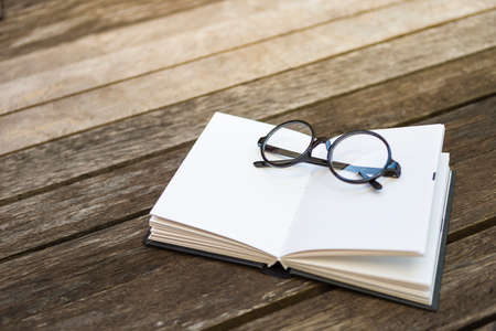Reading glasses on blank notebook on wooden floor, outdoor day light, education conceptの写真素材