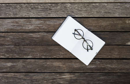 Design black frame eyeglasses on blank notebook with space on old wood background, education concept, outdoor day lightの写真素材