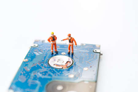 Miniature worker in safty suit on hard disk drive on white background, computer specialist, computer repair and maintenance, service and spare partの写真素材