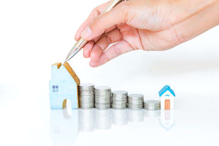 Girl hand holding silver pen pointing on miniature house with stack of coin on white background,...
