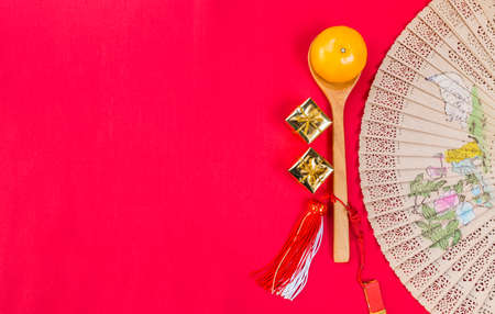 Fresh orange fruit on wooden spoon with golden gift box and wooden hand fan on red fabric background, Chinese new year concept backgroundの写真素材