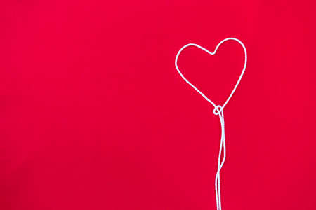 White thread in heart shape on red fabric background, love and romance concept, valentine background ideaの写真素材