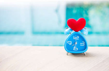 Vintage design blue clock with red heart over blurred blue water background, valentine time, love and romance concept, outdoor day lightの写真素材