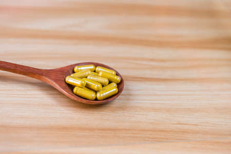 Turmeric powder in vegetable capsule on wooden spoon with space on wood background, herbal medicine, health care productの写真素材