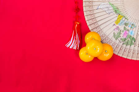 Simple Chinese new year concept background, fresh orange stack and foldable hand fan with space on red fabric backgroundの写真素材