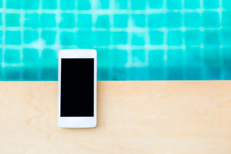 Smartphone on wooden table with space on blurred blue water background, technology concept, outdoor day light, clear communication, swimming pool mobile controlの写真素材