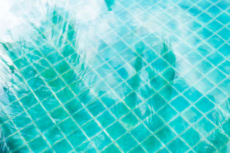 Abstract coconut leaves reflection on swimming pool water, blurred blue water texture background, outdoor day lightの写真素材