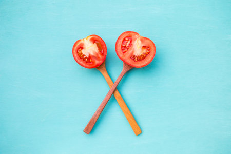 Fresh slice of tomato on wooden spoon on blue background, healthy life styleの写真素材