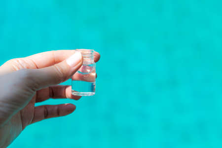 Clear water in small glass bottle in girl hand over blurred blue water background, outdoor day...