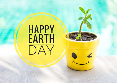 Happy Earth day with smiling yellow plant pot over blurred blue water backgroundの写真素材