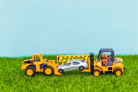 Car insurance concept, truck moving car with work in progress sign on green grass with space on blurred blue background, car service and repair serviceの写真素材