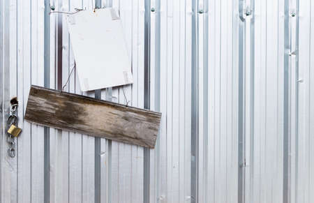 Old wooden sign and white plastic board hanging on metal sheet wall, construction industry, blank sing at construction siteの写真素材