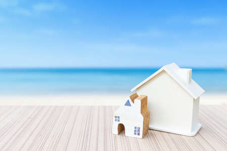 Wooden house model on wooden table over blurred beach background, property business concept, house loanの写真素材